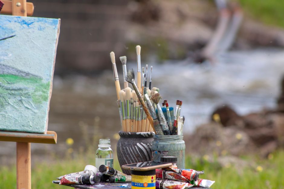 Art materials including brushes, canvas, and paints by a riverside, ideal for creative inspiration.