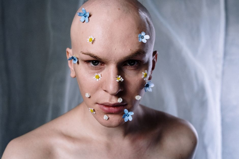 Artistic portrait of a bald man with flower makeup, emphasizing creativity and expression.
