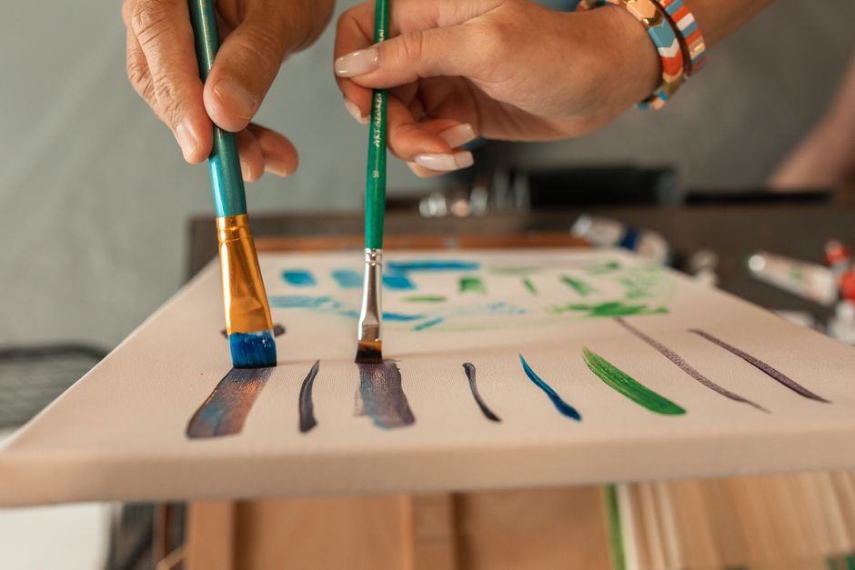 Close-up of hands painting colorful strokes on a canvas, showcasing creativity and technique.